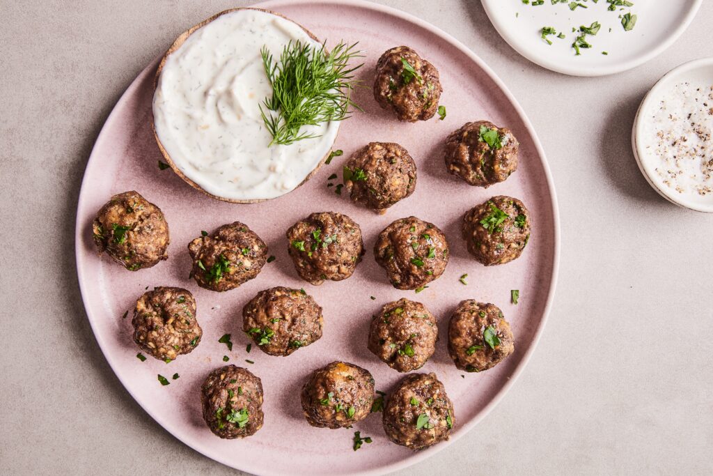 Cooked Moroccan meatballs served on a plate with yogurt dipping sauce on the side.