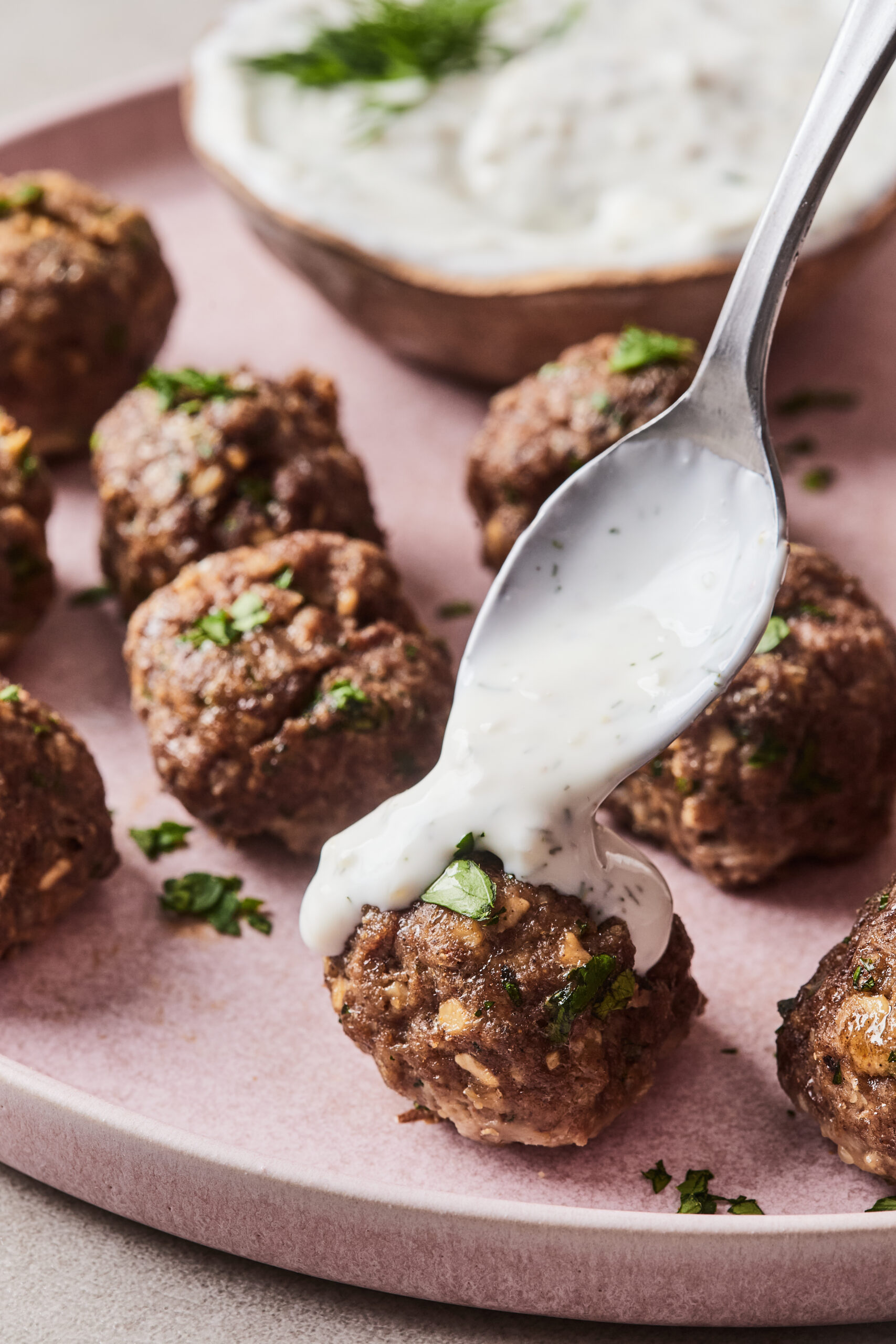 Moroccan meatballs on a plate drizzled with yogurt sauce.