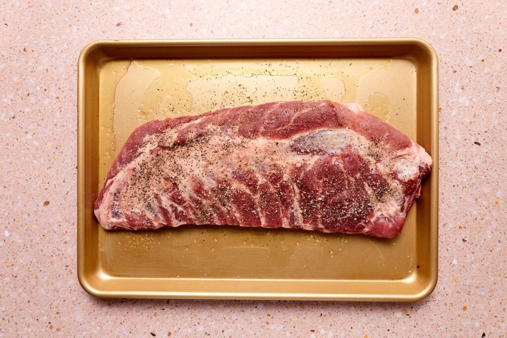 Pork spare ribs sprinkled with salt and pepper on baking sheet.