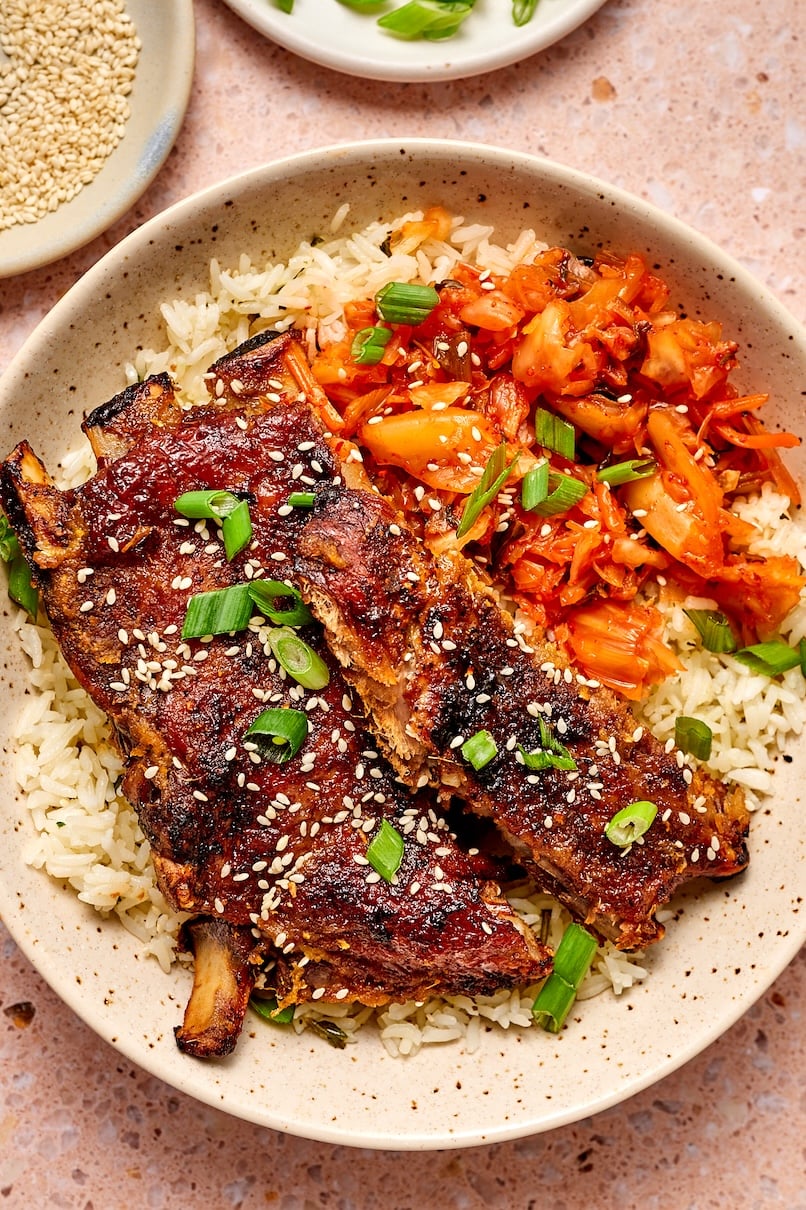 Korean pork ribs in a bowl on top of rice alongside kimchi.