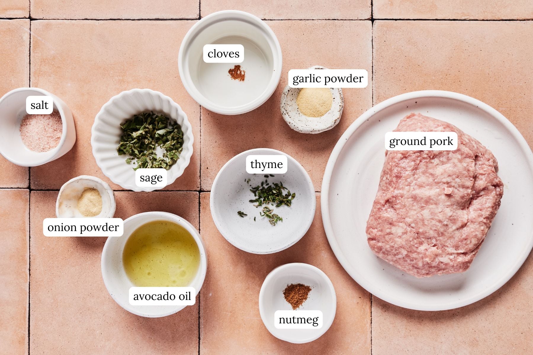 Ingredients for breakfast pork sausage laid out and labeled on a pink tiled countertop.