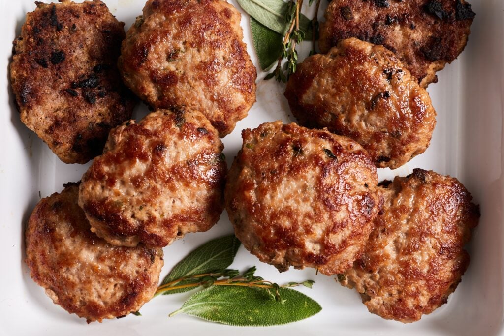 Cooked breakfast sausage on a plate and garnished with sage and thyme