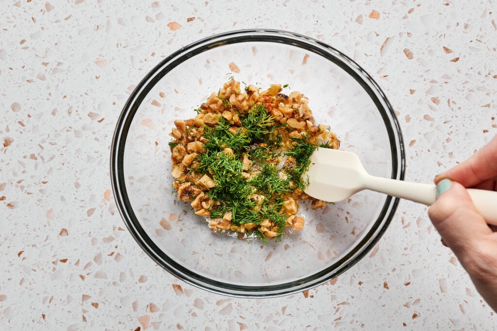 Mixing dill walnut topping together in a bowl.