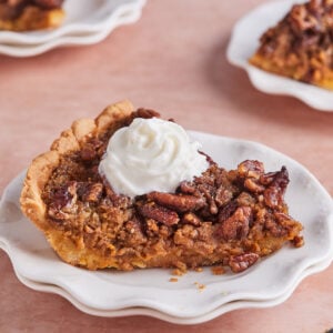 A slice of pumpkin pecan pie on a white plate topped with a dollop of whipped cream