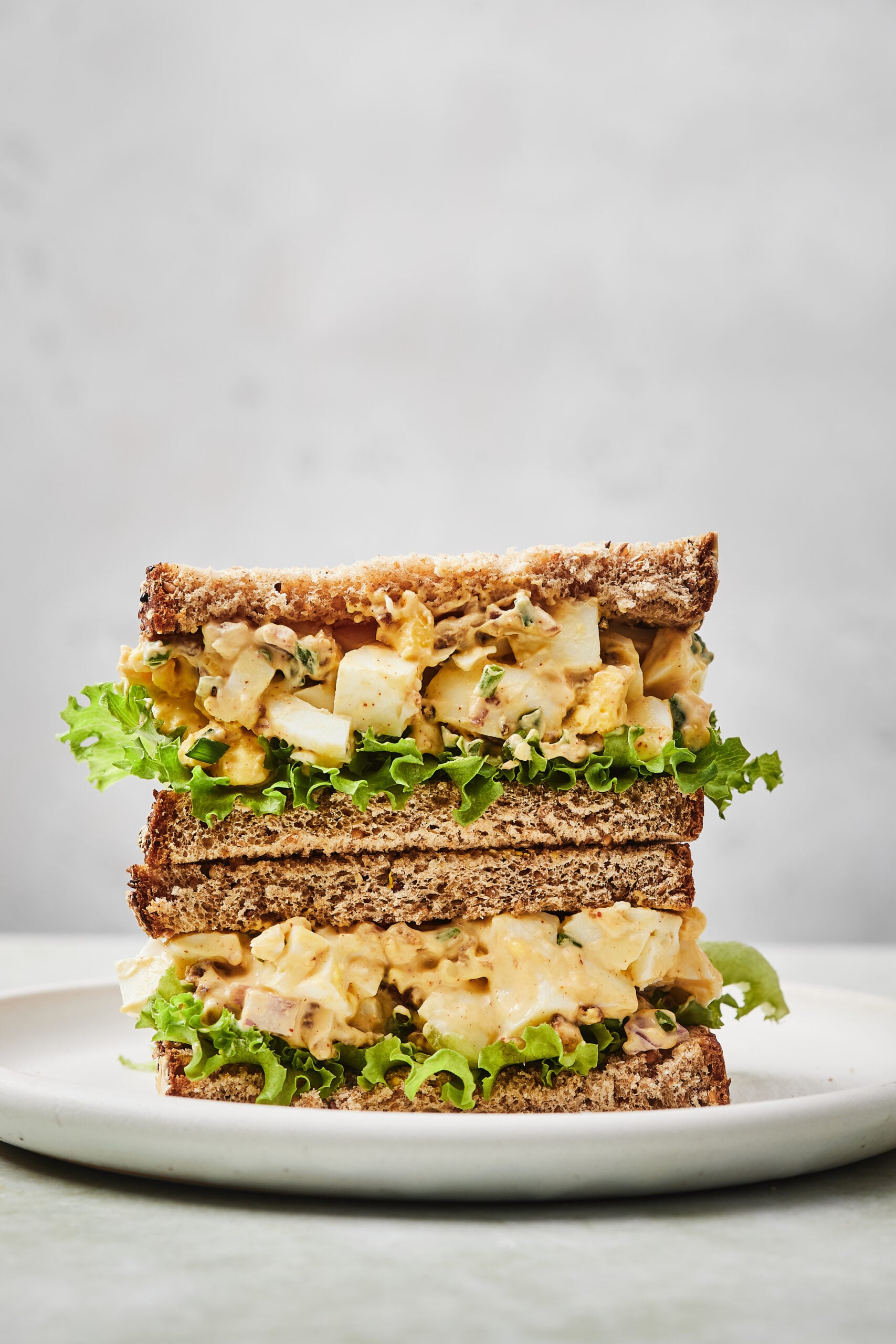 Egg salad sandwich sliced in half and stacked on a white plate.