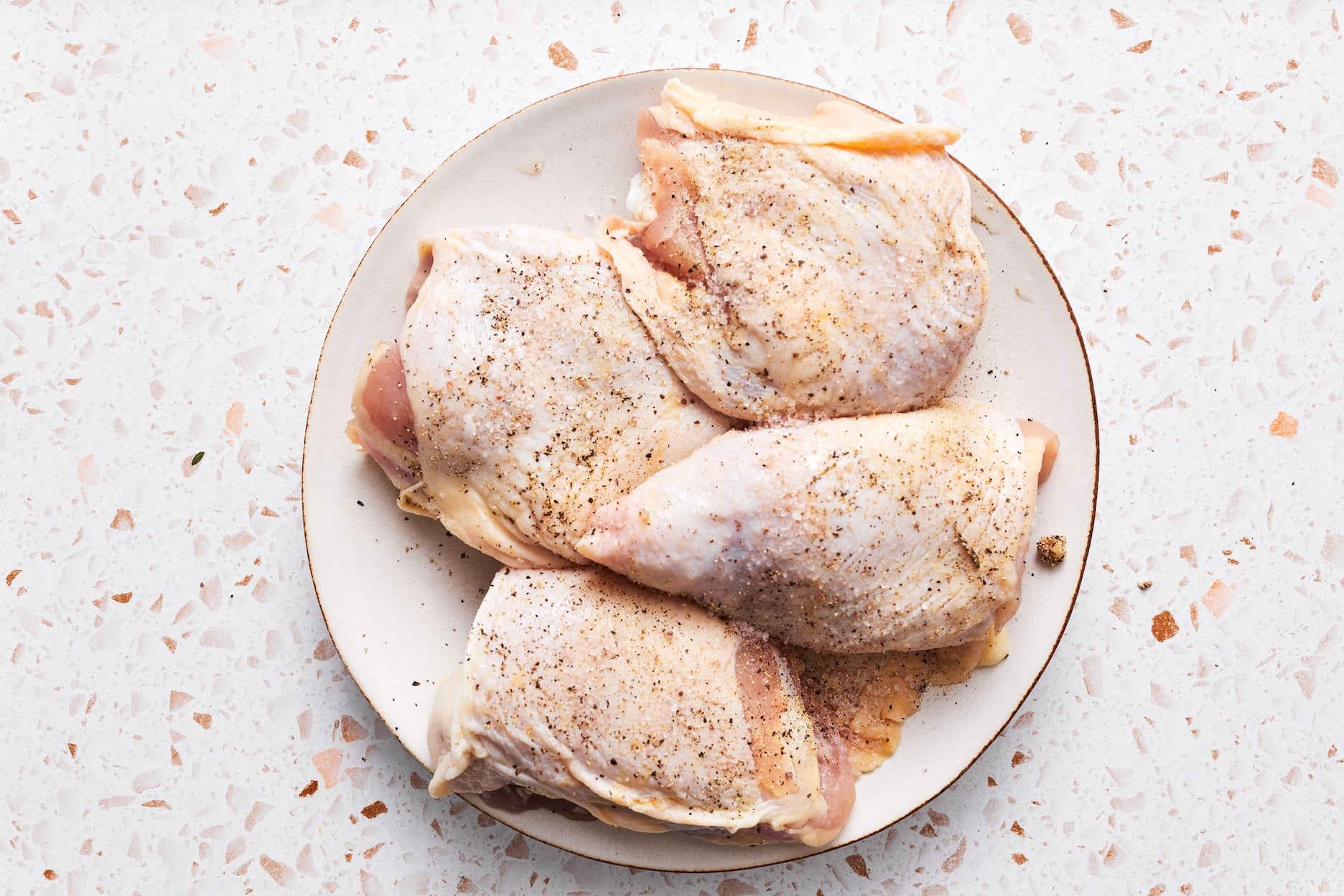 Chicken thighs on a plate seasoned with salt and pepper.