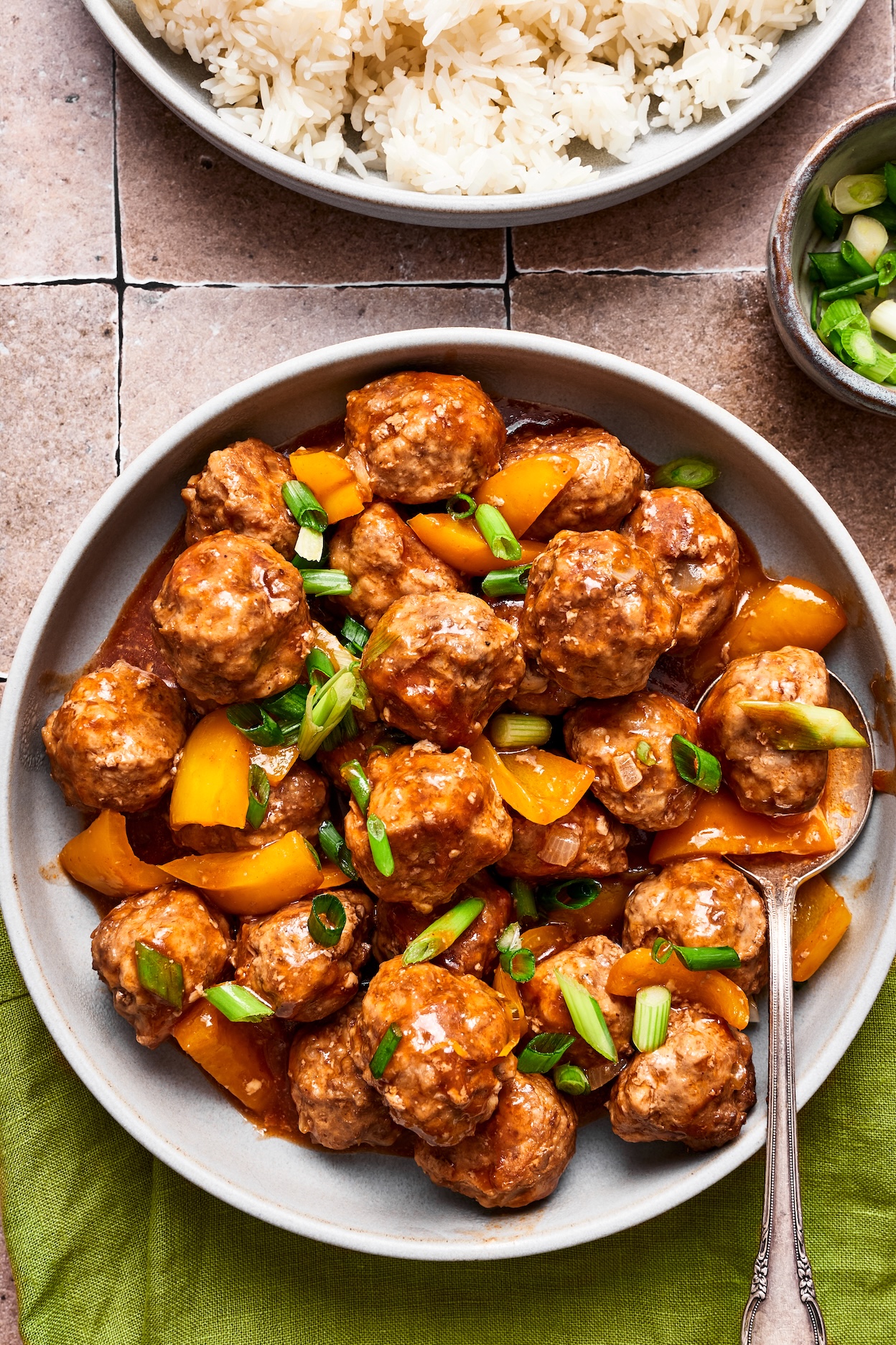 Healthy sweet and sour meatballs in a bowl alongside a bowl of rice and green onions