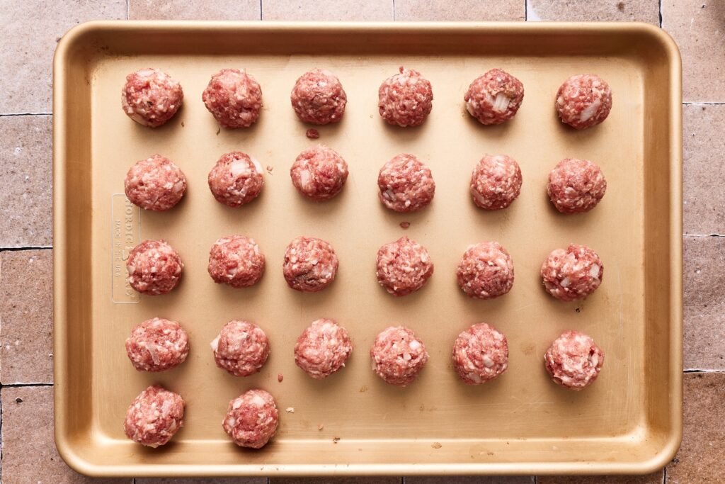 Meatballs shaped and placed on a baking sheet, ready to be baked