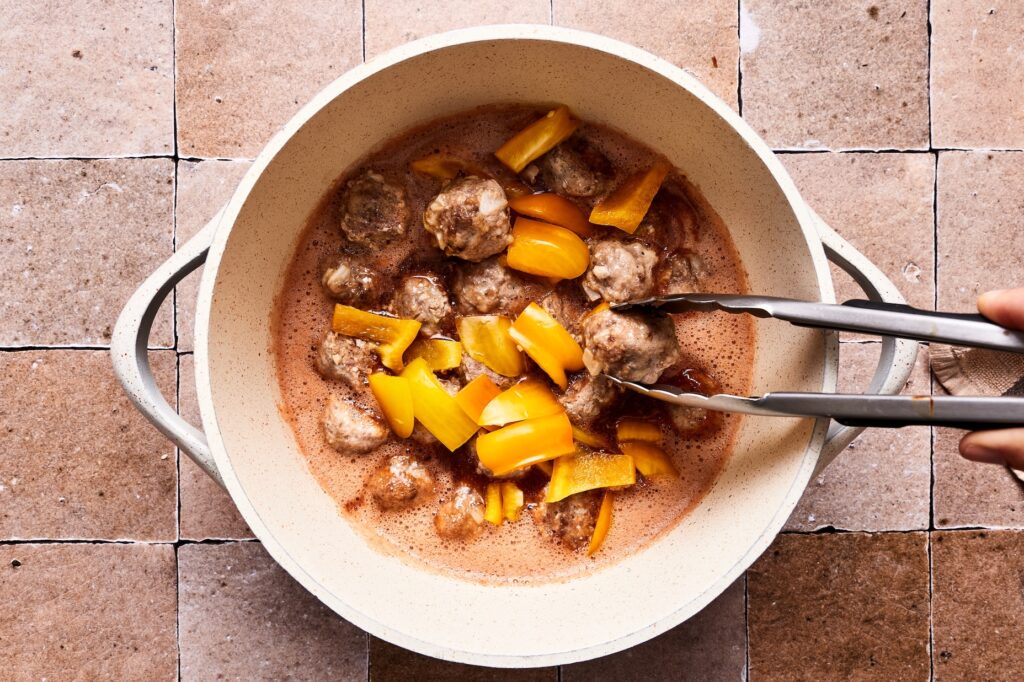 Adding cooked meatballs and bell peppers into cooked sweet and sour sauce