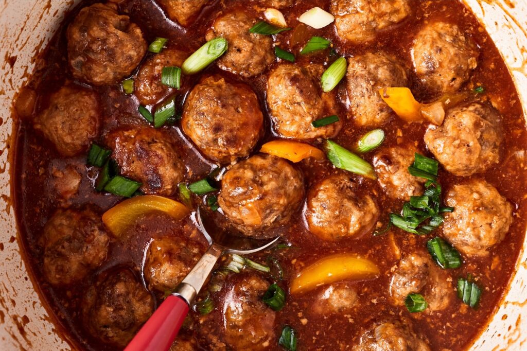 Sweet and sour meatballs in a saucepans cooked and garnished with green onions