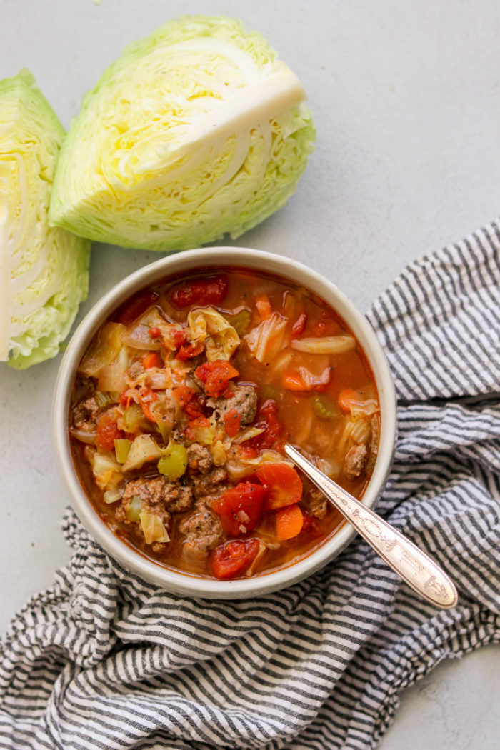 an overhead shot of cabbage soup with ground beef with a silver spoon next to a striped napkin 