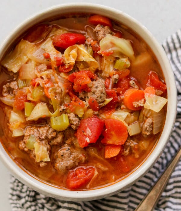 a while bowl filled with cabbage soup next to a silver spoon and striped napkin