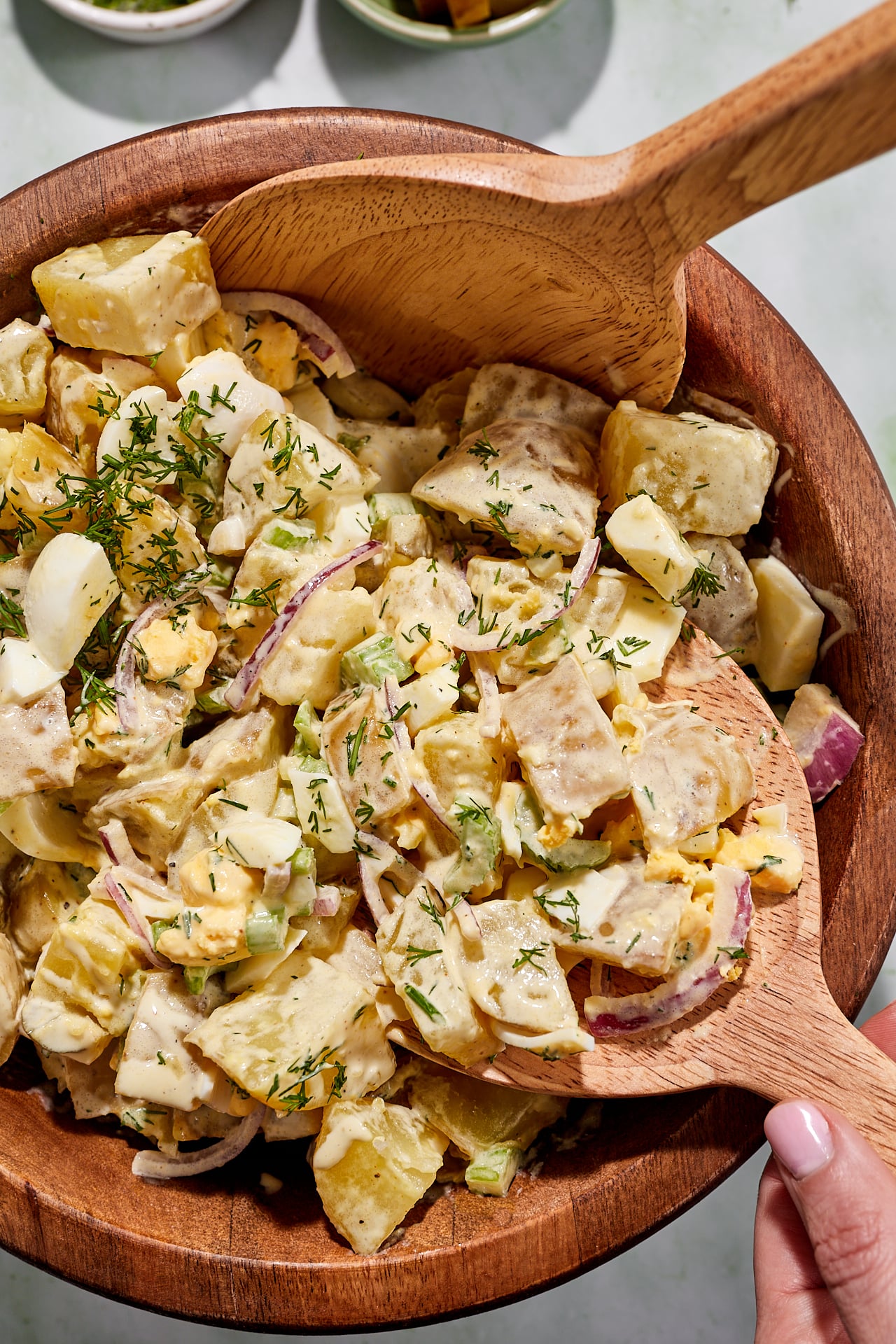 Tossing potato salad in a large wooden bowl