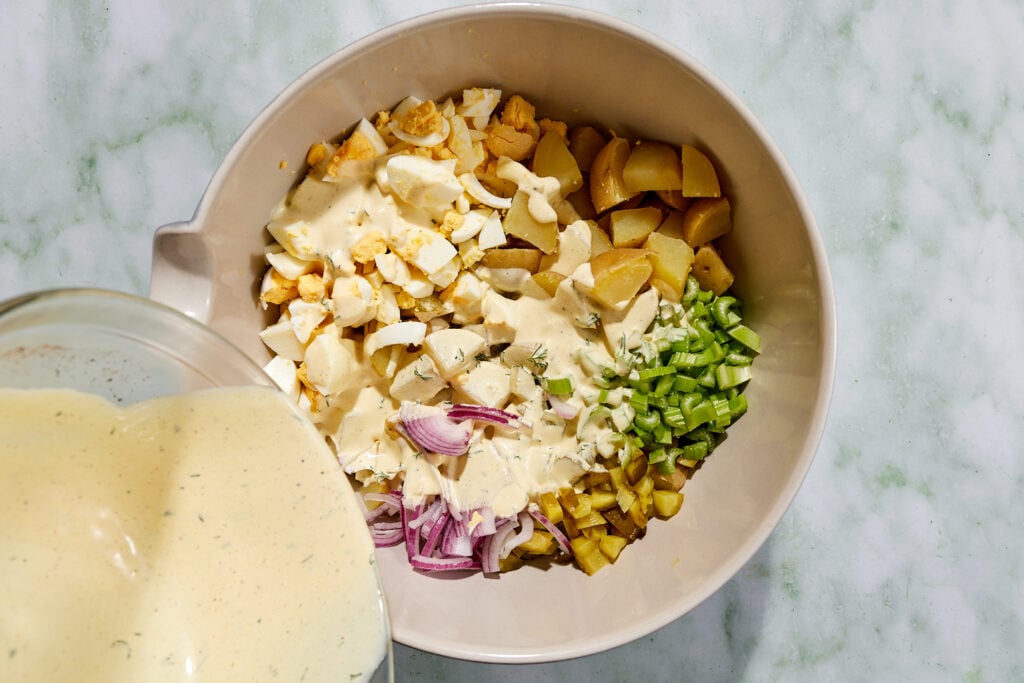 Pouring dressing over the potatoes and vegetables to make potato salad