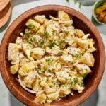 Whole30 dill pickle potato salad in a large wooden bowl, garnished with dill