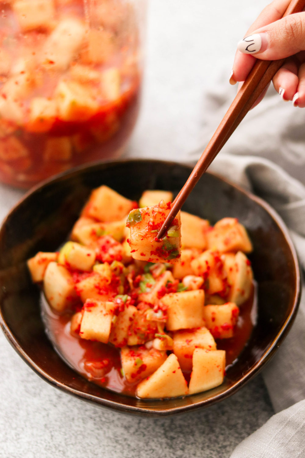 a bowl of korean radish kimchi in a small brown bowl with chopsticks picking up a piece. 