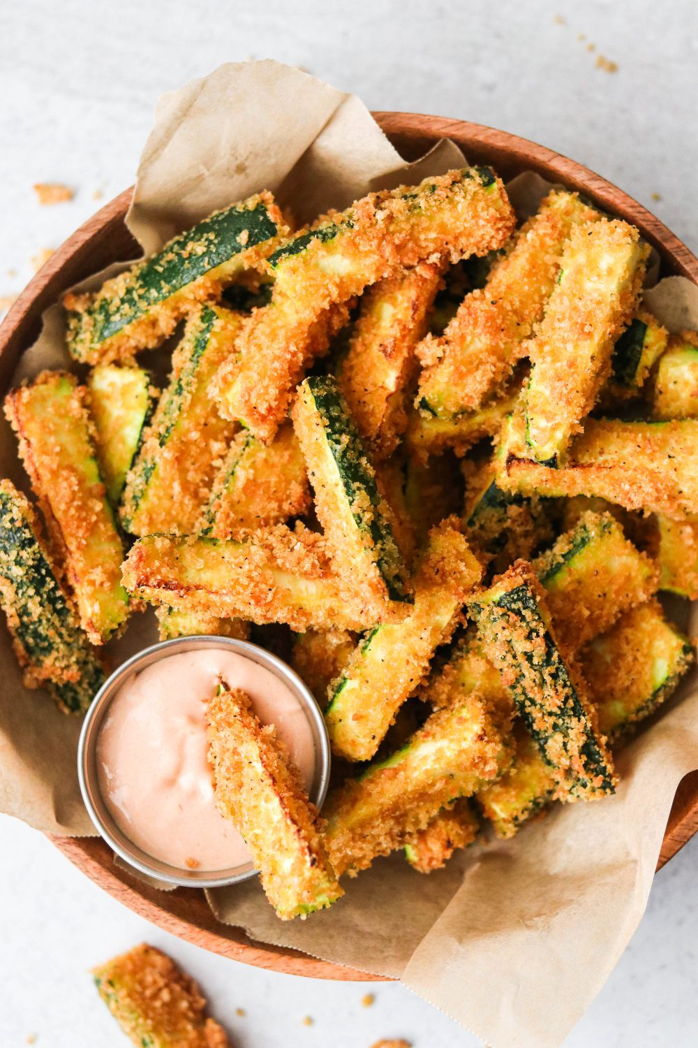 an overhead shot of air fryer zucchini fries in a brown bowl with one dipping into a sauce. 