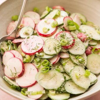 a creamy cucumber radish salad in a white bowl topped with fresh dill and green onions