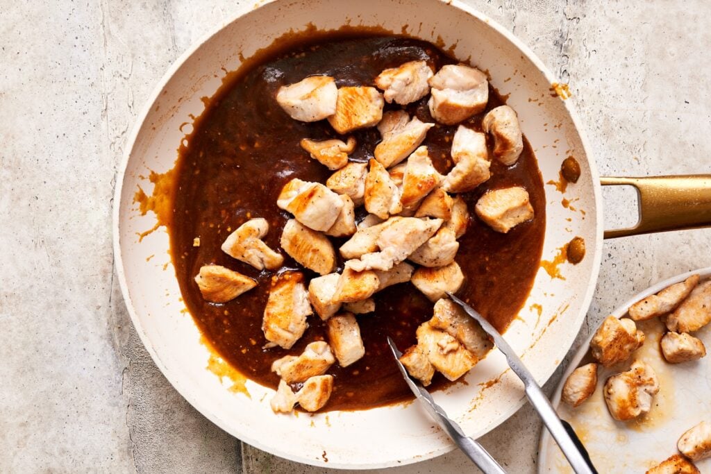 Adding cooked chicken to the skillet with simmered teriyaki sauce
