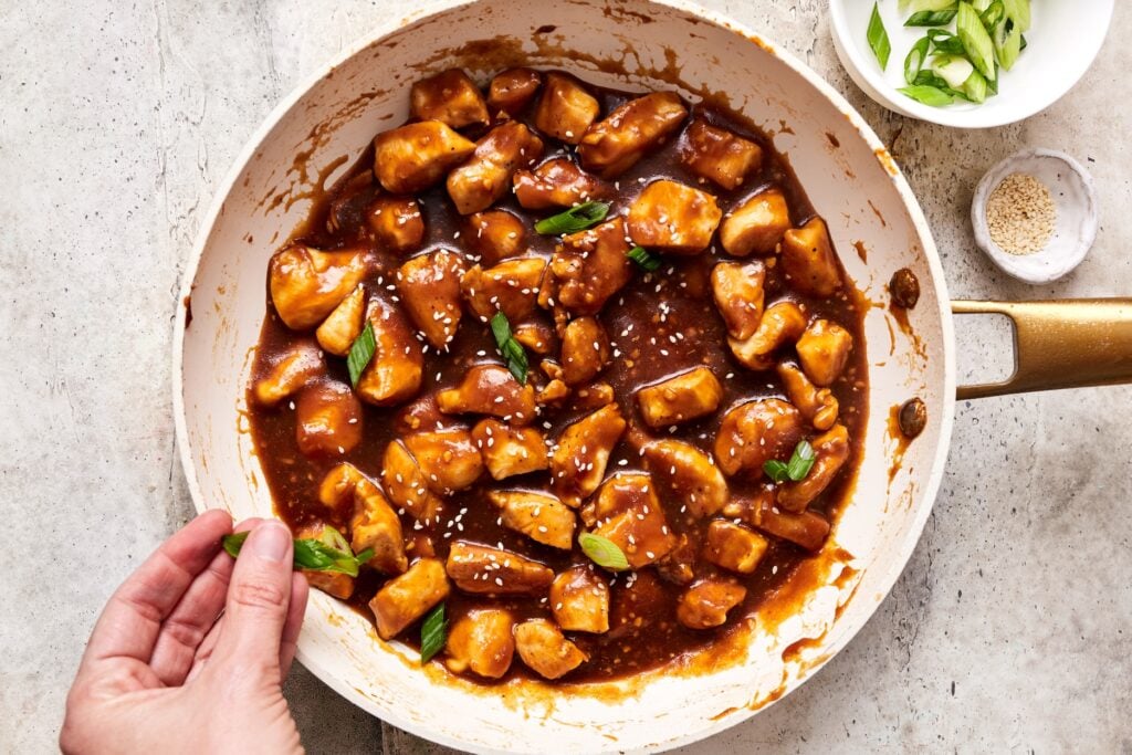 sprinkling pineapple teriyaki chicken with sesame seeds and green onions