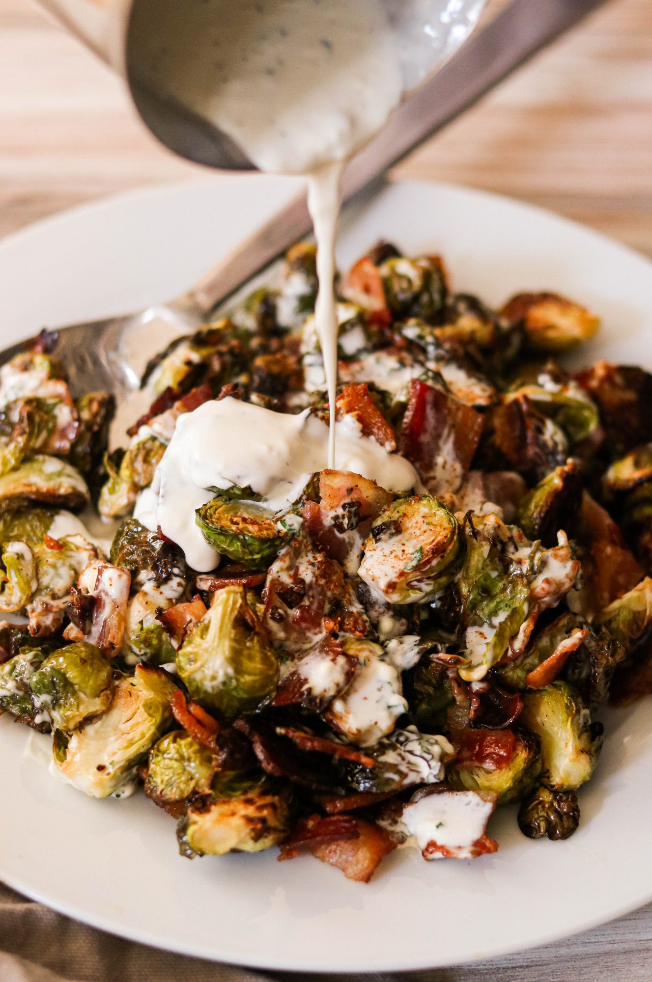 a ladle drizzling ranch dressing over keto brussels sprouts with bacon