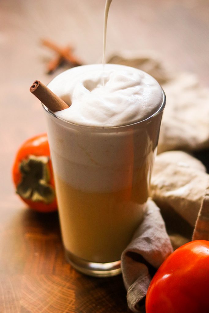 persimmon latte in a glass with frothed milk being poured on top