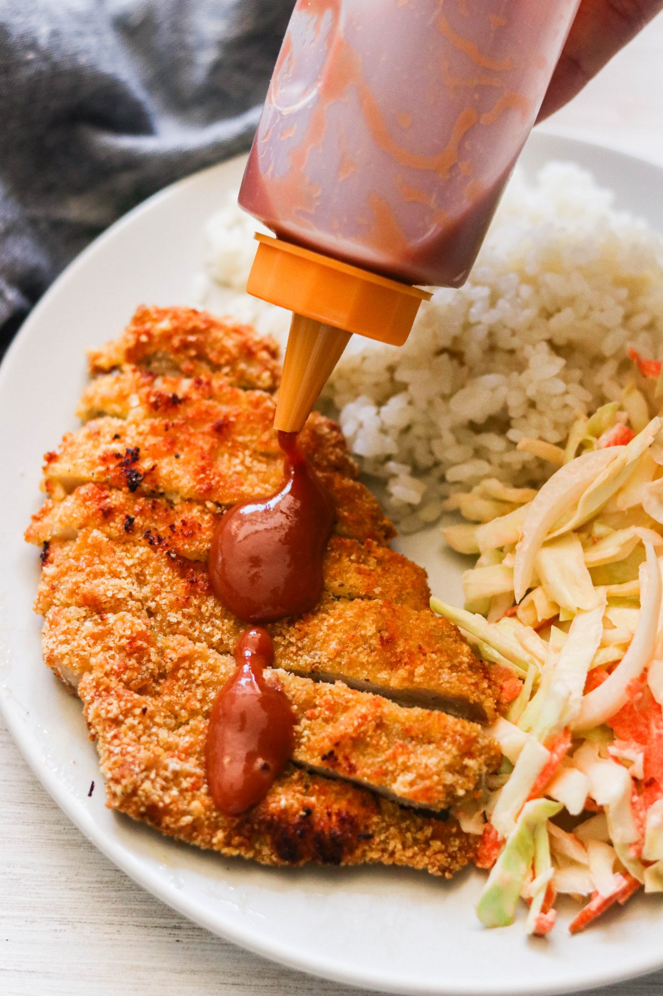 a bottle of tonkatsu sauce drizzled over a pork cutlet 