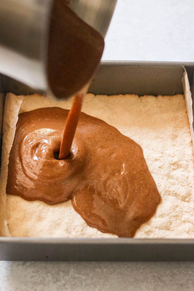 Pouring caramel sauce over shortbread layer to make homemade twix bars