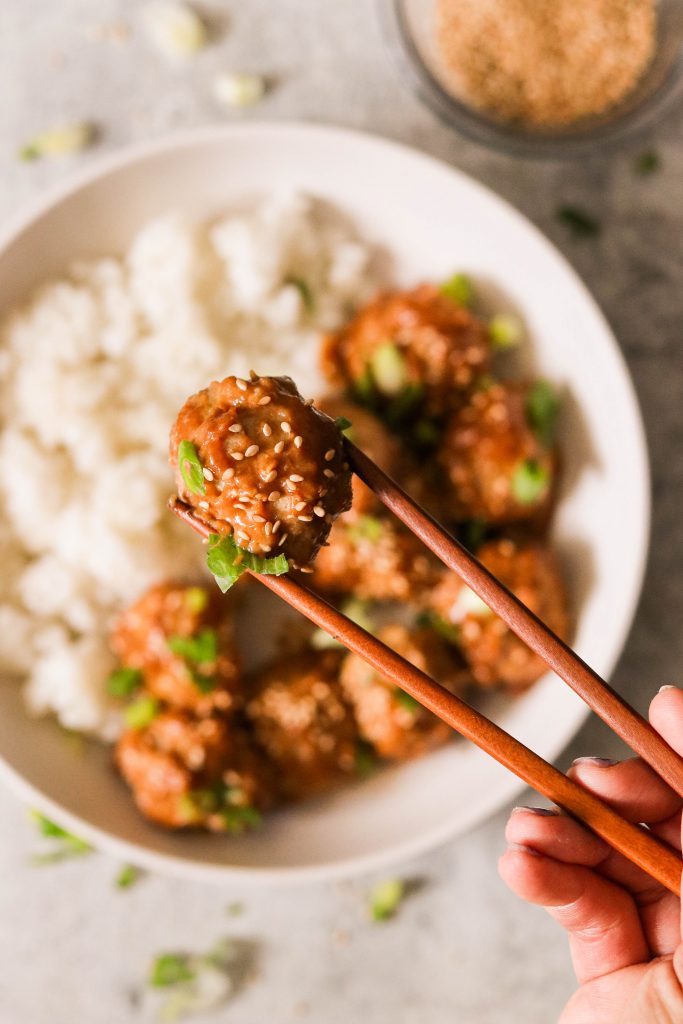 a close up of whole30 chicken meatballs held up with chopsticks