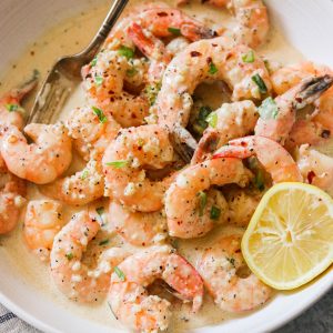 creamy garlic shrimp in a bowl with a fork and lemon