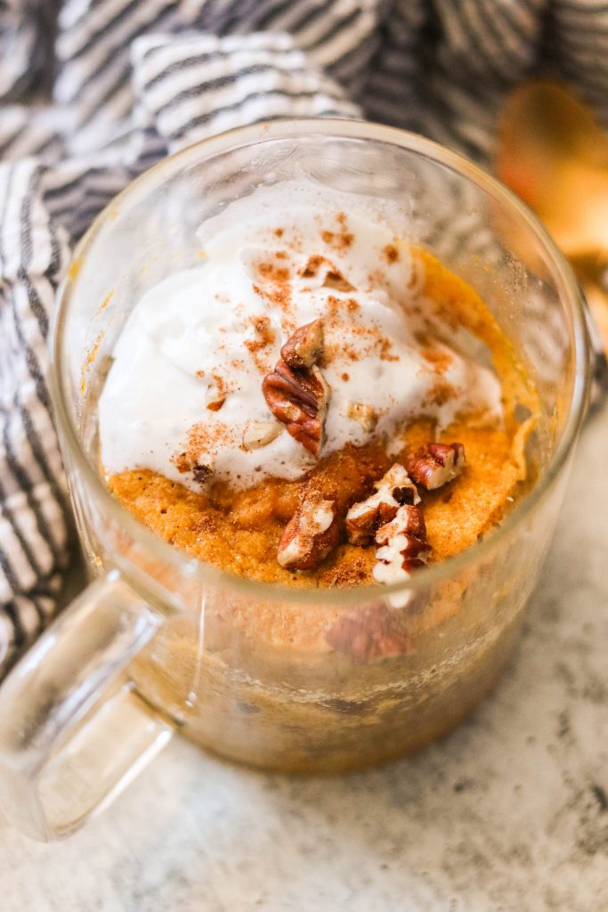 paleo pumpkin mug cake topped with whipped coconut cream, pecans, and pumpkin pie spice