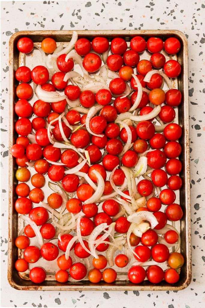 tomatoes, onions, and garlic on a baking sheet, ready to be roasted