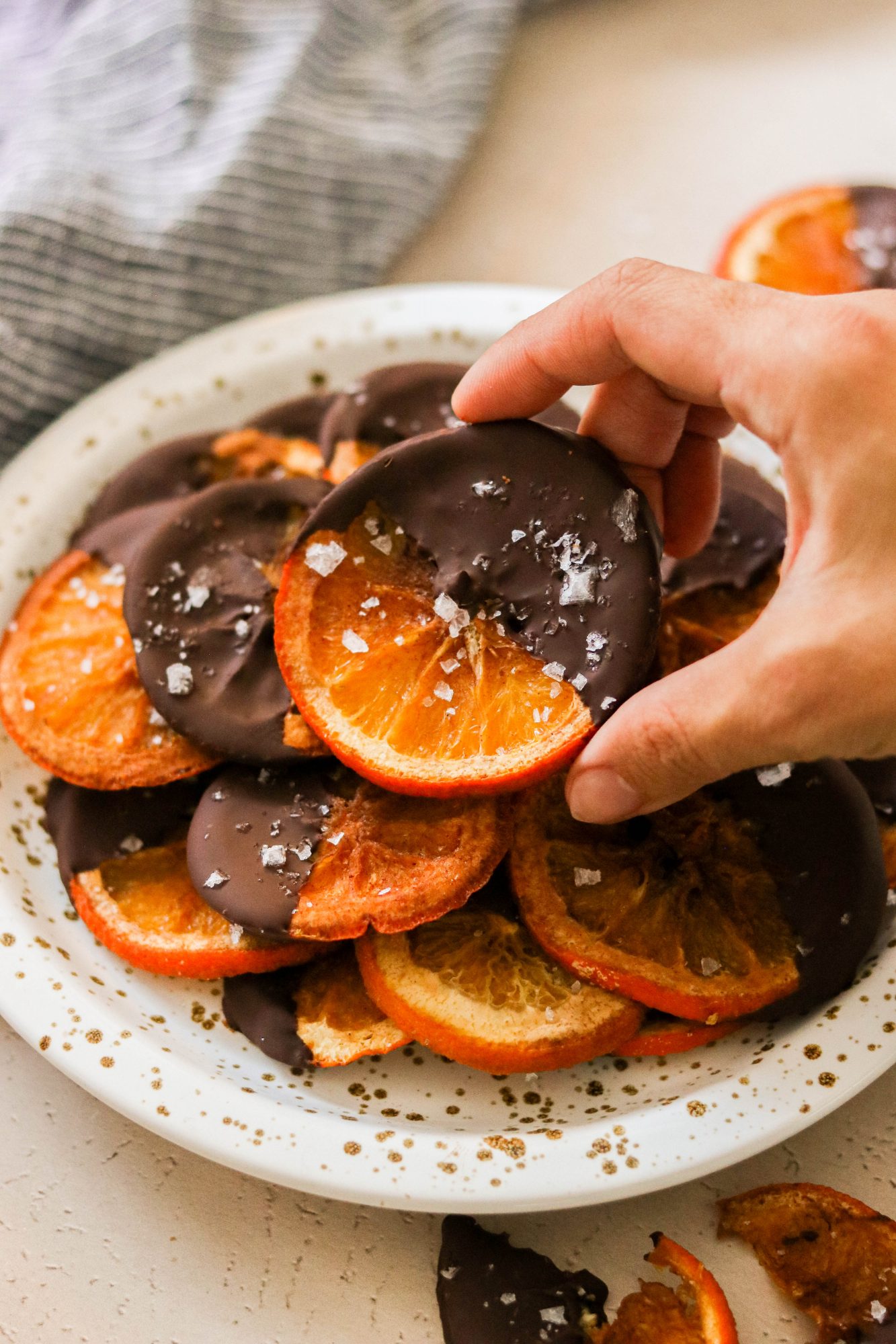 reaching for a dark chocolate covered orange slices on a plate