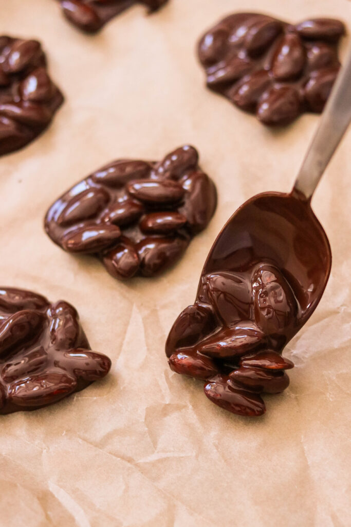 Placing mounds of dark chocolate almond clusters on parchment paper