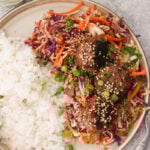 Egg roll meatballs served on a gray plate with white rice and sesame slaw, garnished with green onions and toasted sesame seeds.