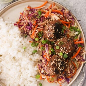 Egg roll meatballs served on a gray plate with white rice and sesame slaw, garnished with green onions and toasted sesame seeds.