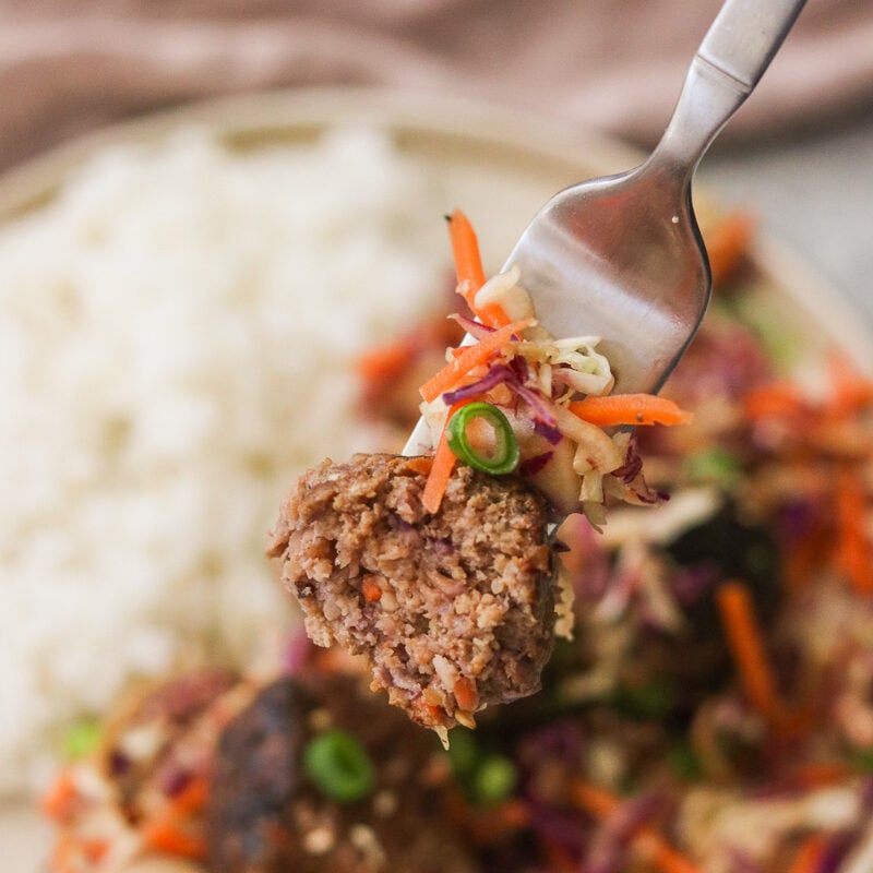 Egg roll meatball on a fork with a bite taken out, revealing the juicy center.