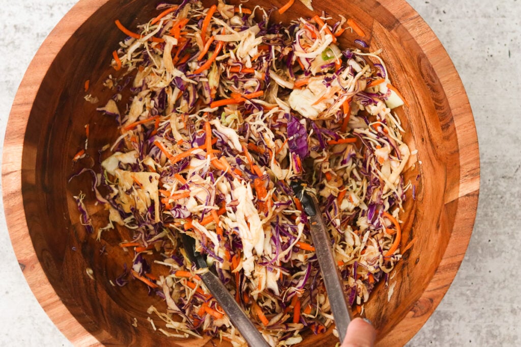 Coleslaw tossed together in a large bowl with egg roll sauce.