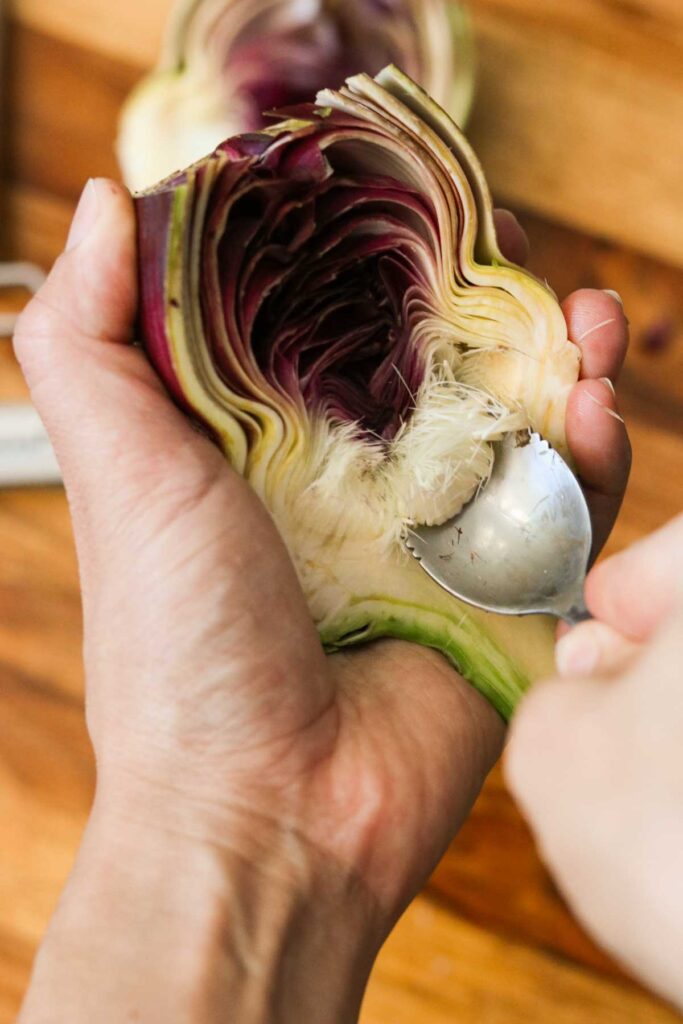 Scooping out the fuzzy choke of an artichoke with a grapefruit spoon