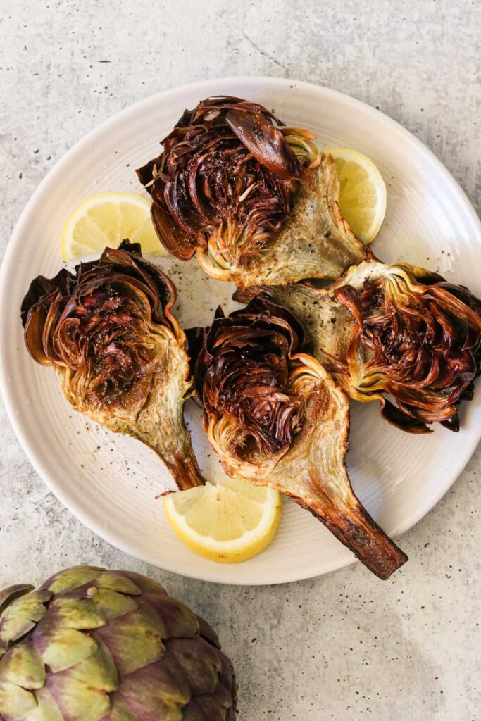 Fried artichokes served on a plate with salt, pepper, and lemon wedges.