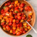 Blistered cherry tomatoes in a wooden bowl with a silver spoon.