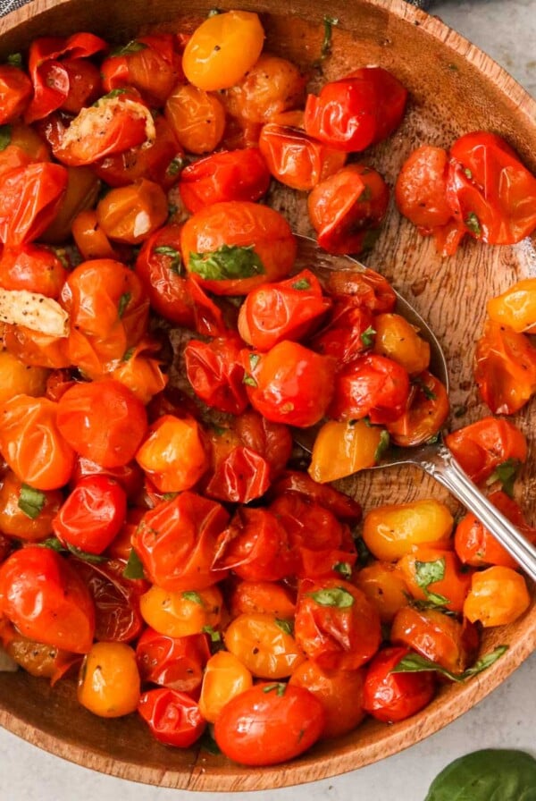 Blistered cherry tomatoes in a wooden bowl with a silver spoon.