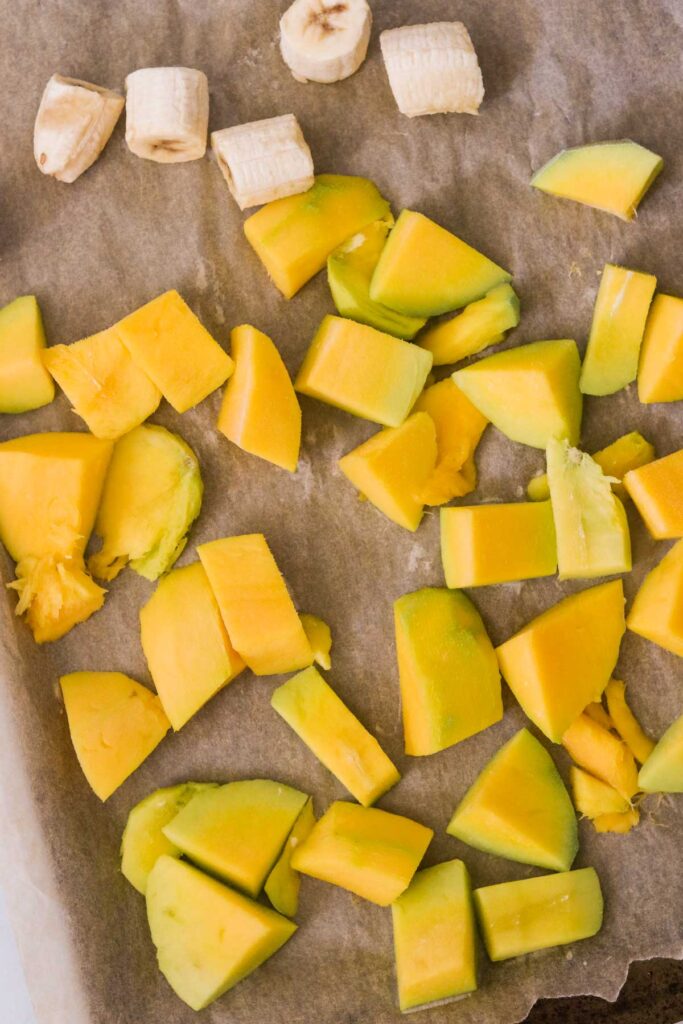 Cut up mangos and banana on a baking sheet, ready to be frozen.