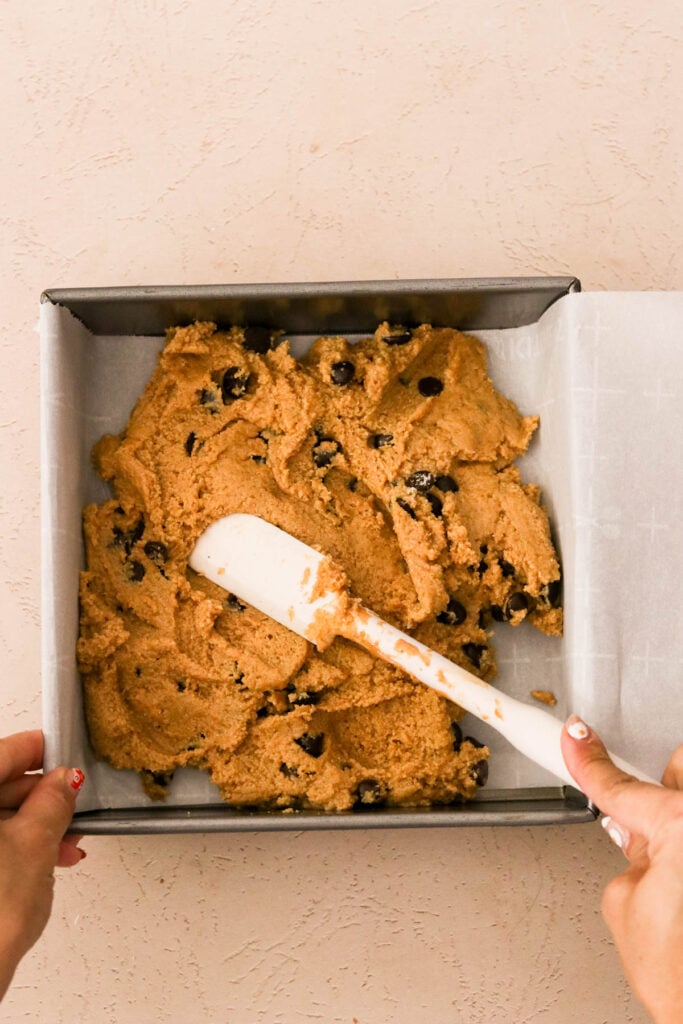 Spreading peanut butter bar batter into a parchment lined square pan