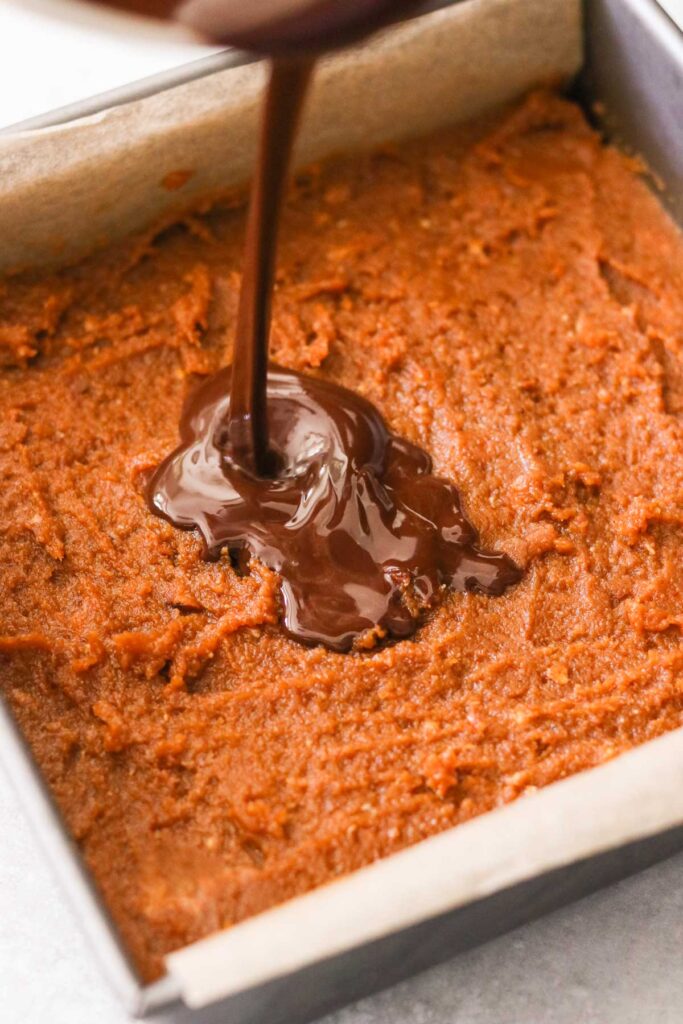 Pouring melted chocolate over pumpkin mixture in a baking pan