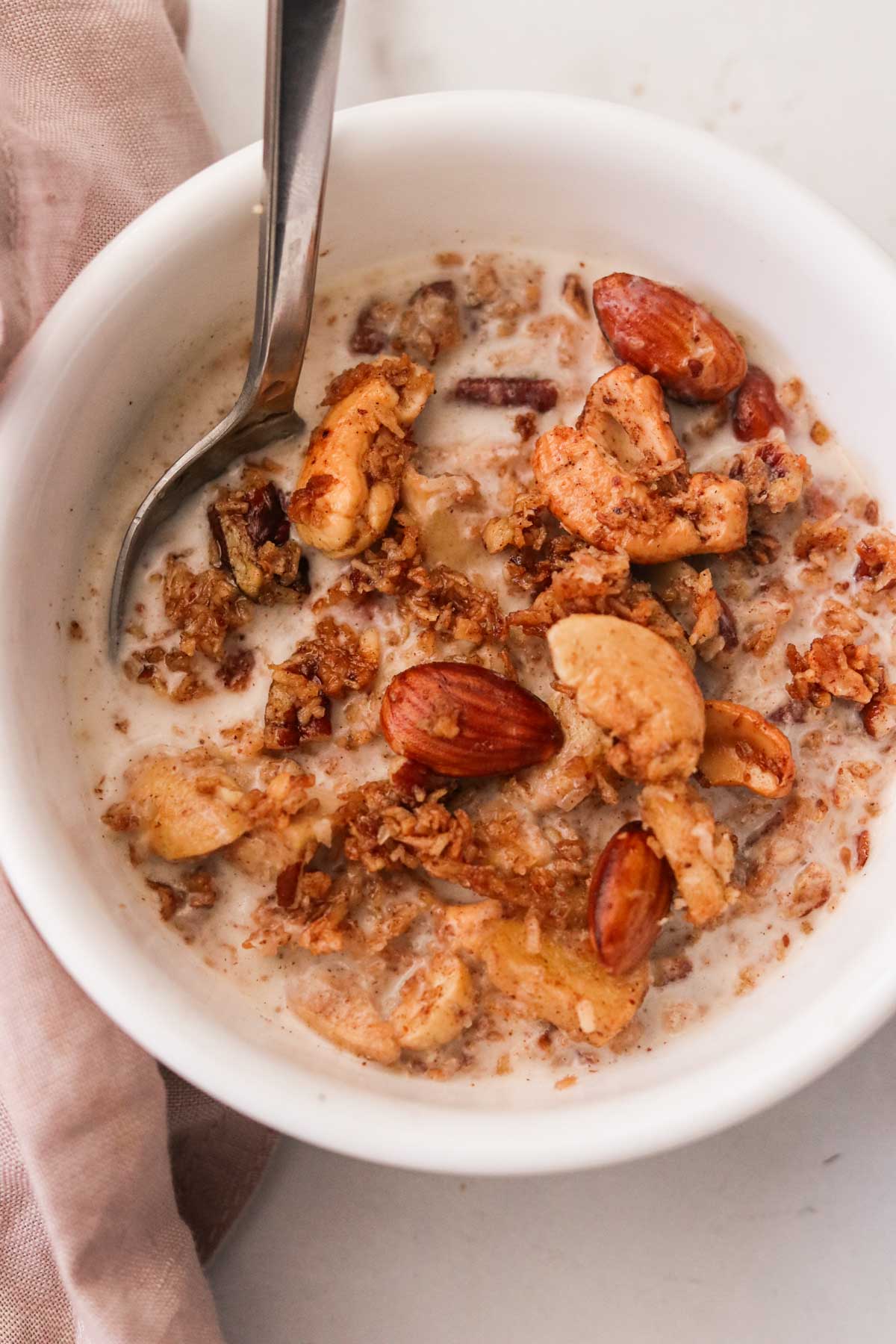 granola in a white bowl with milk and a silver spoon