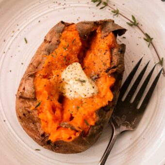 an overhead shot of a baked sweet potato topped with butter and fresh herbs and seasonings