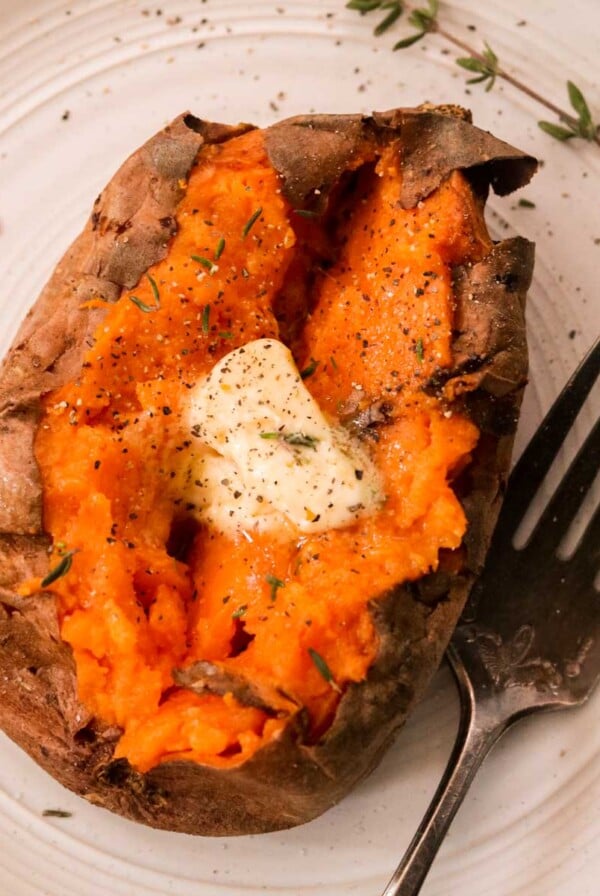 an overhead shot of a baked sweet potato topped with butter and fresh herbs and seasonings