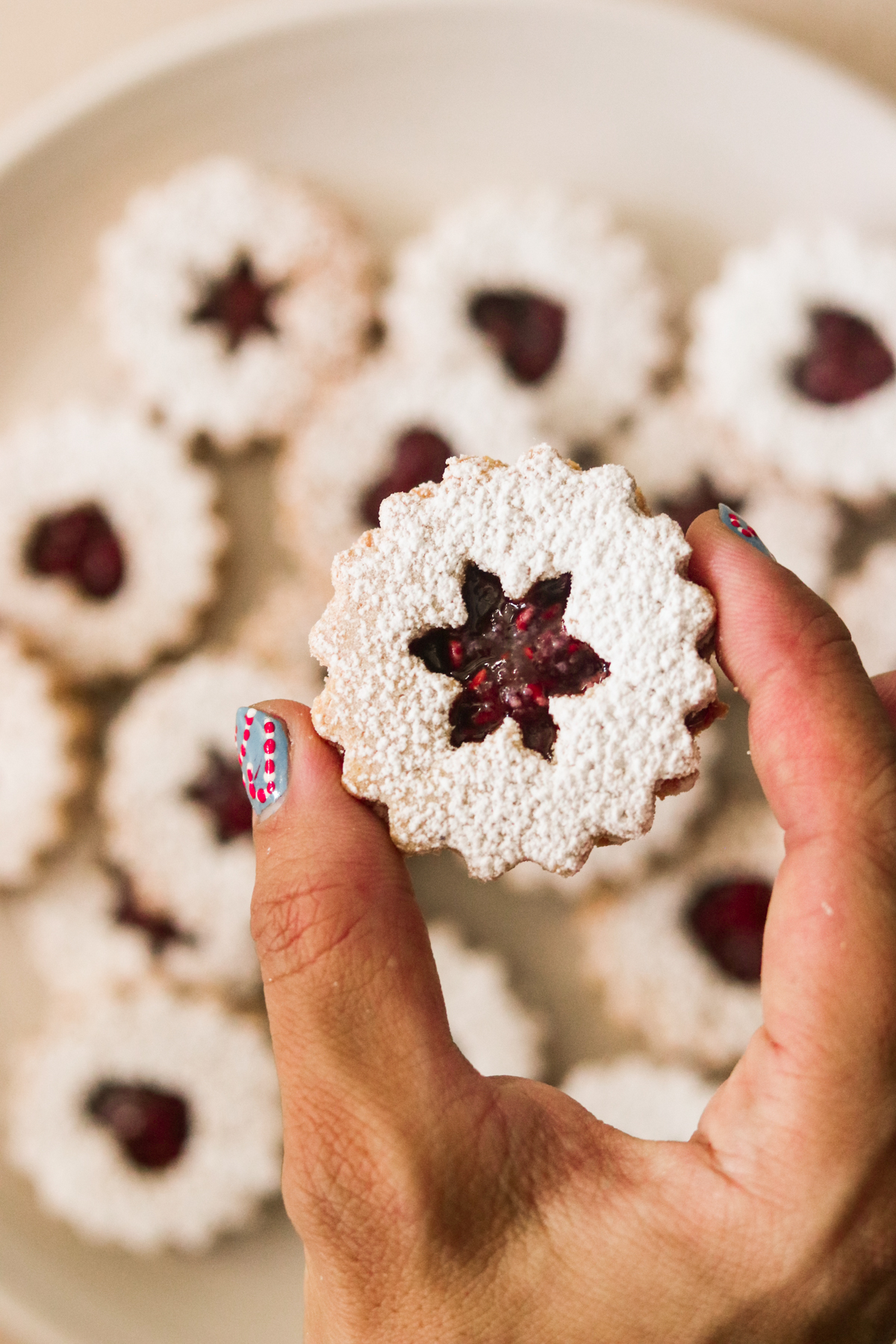 a hand holding a linzer cookie with a snowflake shape in the center