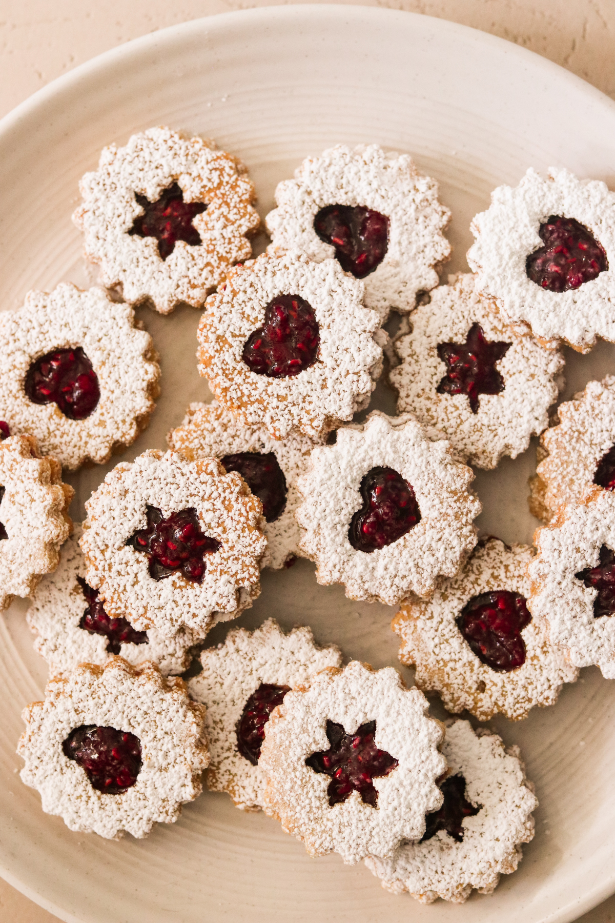 an overhead shot of linzer augen cookies on a white plate filled with homemade raspberry jam and dusted with powdered sugar